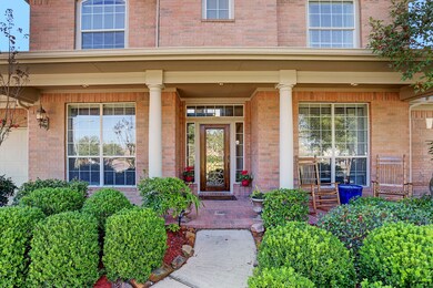 Cozy covered porch with brick pavers and stately columns surrounded by lush landscaping.