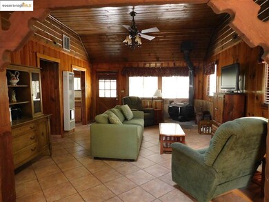 Tiled living room featuring wood ceiling, wood walls, a wood stove, lofted ceiling, and ceiling fan