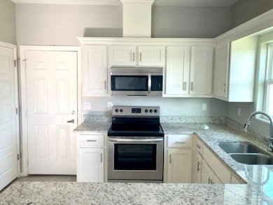 Kitchen featuring stainless steel appliances, white cabinetry, and light stone counters
