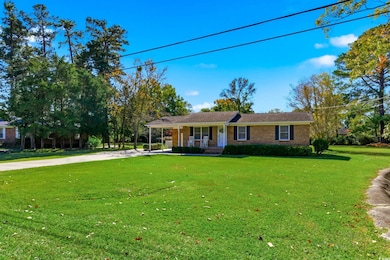 Ranch-style home with covered porch, driveway, a front yard, brick siding, and an attached carport