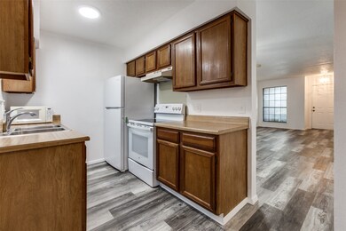 Kitchen featuring white appliances, light wood-style floors, under cabinet range hood, light countertops, and brown cabinetry