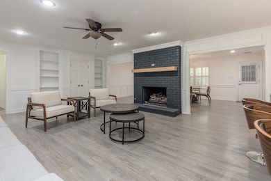 Living area featuring a decorative wall, built in shelves, ceiling fan, a fireplace, and crown molding