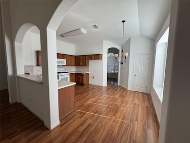 Kitchen featuring arched walkways, light countertops, decorative backsplash, a chandelier, and brown cabinets