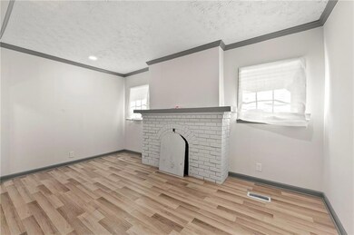 Unfurnished living room featuring ornamental molding, a textured ceiling, wood finished floors, a brick fireplace, and baseboards