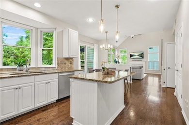 Kitchen featuring dishwasher, a sink, stone counters, a chandelier, and dark wood-style floors