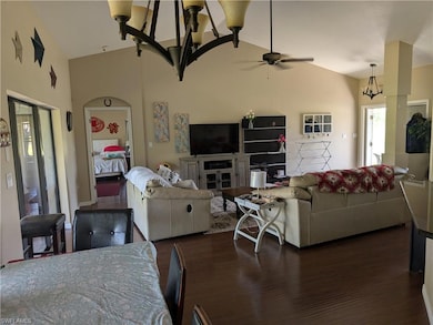 Living room with vaulted ceiling, ceiling fan, dark wood-style flooring, and a chandelier