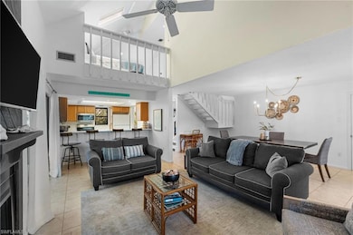 Living room with ceiling fan with notable chandelier, a healthy amount of sunlight, a towering ceiling, and light tile patterned floors