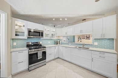 Chic, coastal vibe kitchen with glass-front cabinets, gas range, sleek backsplash, and under-cabinet lighting.