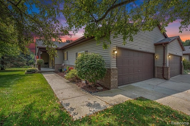 View of property hidden behind natural elements with a lawn, brick siding, driveway, and an attached garage