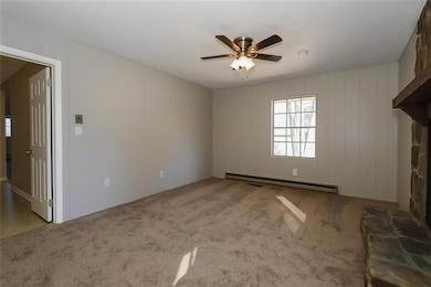 Unfurnished living room with light carpet, a baseboard radiator, a ceiling fan, and a fireplace