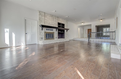 Unfurnished living room with a stone fireplace, dark wood-type flooring, crown molding, and recessed lighting