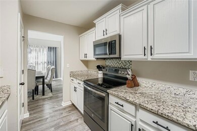Kitchen featuring stainless steel appliances, white cabinetry, light stone counters, and backsplash