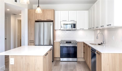 Kitchen with a sink, appliances with stainless steel finishes, light brown cabinetry, light wood-style floors, and decorative backsplash