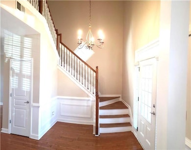 Stairway featuring wood finished floors, wainscoting, a chandelier, a high ceiling, and a decorative wall