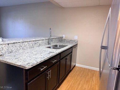 Kitchen with freestanding refrigerator, light stone countertops, light wood-style floors, a peninsula, and a paneled ceiling