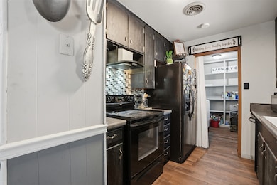 Kitchen featuring black appliances, light wood-type flooring, backsplash, and dark brown cabinetry