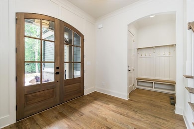Entrance foyer featuring arched walkways, ornamental molding, french doors, light wood finished floors, and baseboards