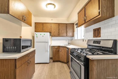 Kitchen featuring stainless steel appliances, brown cabinetry, light wood-style flooring, decorative backsplash, and light countertops