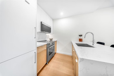 Kitchen with a peninsula, light stone counters, light wood-style floors, stainless steel appliances, and a breakfast bar area