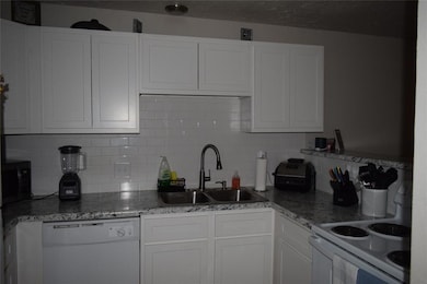 Kitchen featuring white appliances, tasteful backsplash, white cabinets, and light stone counters