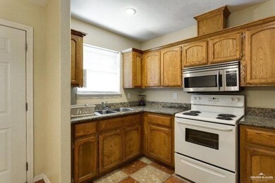 Kitchen with a sink, brown cabinetry, white electric range oven, stainless steel microwave, and dark countertops