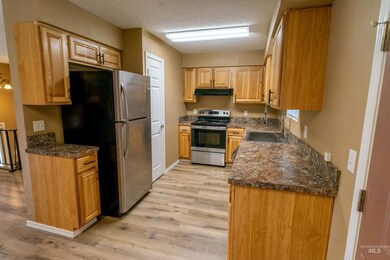 Kitchen with stainless steel appliances, under cabinet range hood, light wood-type flooring, dark countertops, and a textured ceiling