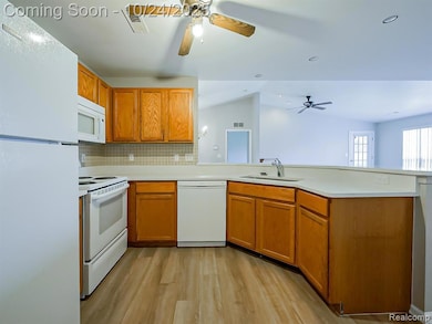 Kitchen with white appliances, tasteful backsplash, light countertops, brown cabinetry, and light wood finished floors