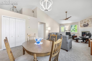 Dining area featuring light colored carpet, a chandelier, a fireplace, ceiling fan, and high vaulted ceiling