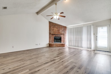 Unfurnished living room featuring a textured ceiling, wood finished floors, a brick fireplace, and a ceiling fan