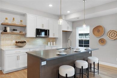 Kitchen featuring white cabinets, backsplash, light wood-style floors, open shelves, and a kitchen bar