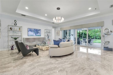 Living room with a tray ceiling, marble tiled flooring, recessed lighting, ornamental molding, and a chandelier