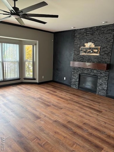 Unfurnished living room featuring ceiling fan, wood finished floors, and a fireplace