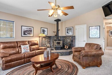 Carpeted living room featuring vaulted ceiling, ceiling fan, and a wood stove