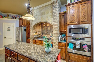 Kitchen with crown molding, gas cooktop, electric microwave and oven appliances with stainless steel finishes, dark stone countertops, a kitchen island, and pendant lighting