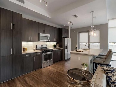 Kitchen with dark wood-type flooring, a wealth of natural light, appliances with stainless steel finishes, and pendant lighting