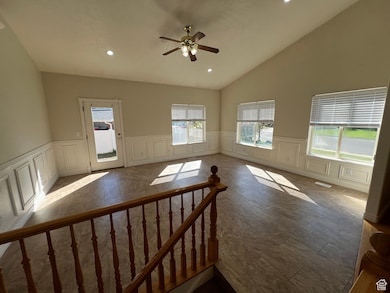 Living room featuring recessed lighting, a decorative wall, a ceiling fan, wainscoting, and high vaulted ceiling