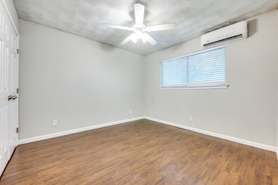 Empty room with a wall mounted air conditioner, a ceiling fan, and wood finished floors