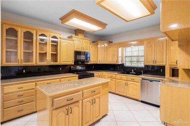 Kitchen with black appliances, light brown cabinets, light tile patterned floors, and tasteful backsplash