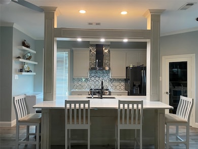Kitchen with ornamental molding, a breakfast bar, light stone counters, tasteful backsplash, and wall chimney range hood