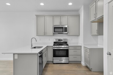 Kitchen featuring a sink, gray cabinetry, a peninsula, stainless steel appliances, and light wood-style flooring