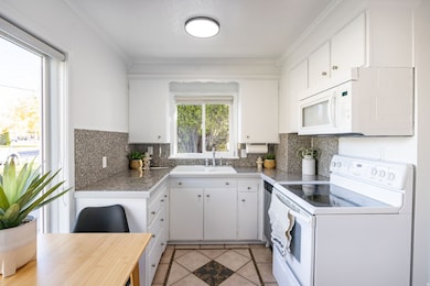 Kitchen featuring white appliances, white cabinets, light tile patterned floors, tile countertops, and ornamental molding