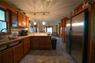 Kitchen with pendant lighting, sink, stainless steel fridge, a textured ceiling, and kitchen peninsula