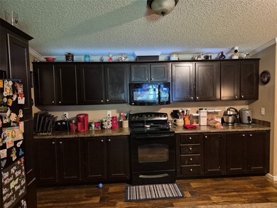 Kitchen with black appliances, dark wood finished floors, a textured ceiling, and crown molding