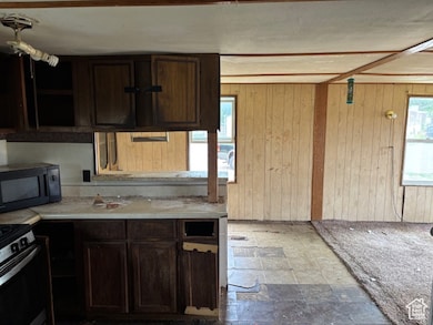 Kitchen featuring healthy amount of natural light, wooden walls, black microwave, light countertops, and dark brown cabinetry