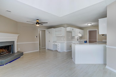 Kitchen featuring decorative backsplash, a ceiling fan, light countertops, a brick fireplace, and white cabinets