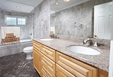Remodeled main bathroom with custom tiled walls and floors, crown molding, granite topped vanity, dual basins, large mirror, designer lighting, frameless glass enclosed tiled tub/shower and privacy window.