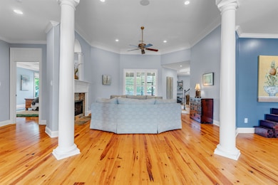 Living room with ceiling fan, hardwood floors, decorative columns, gas fireplace, and recessed lighting.