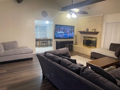 Living room with a brick fireplace, wood finished floors, and a ceiling fan