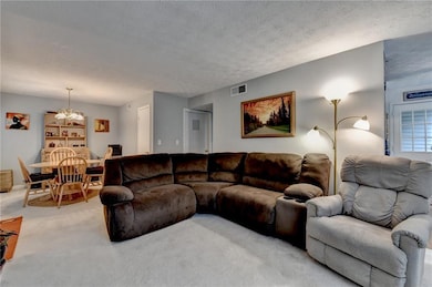 Living area with light colored carpet, a chandelier, and a textured ceiling