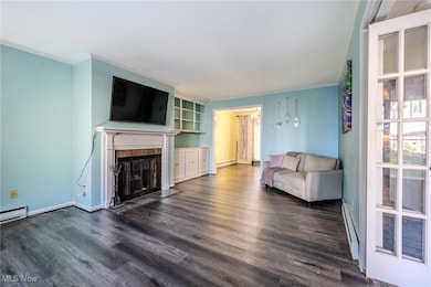 Living area featuring crown molding, baseboard heating, dark wood finished floors, a fireplace with flush hearth, and a baseboard heating unit